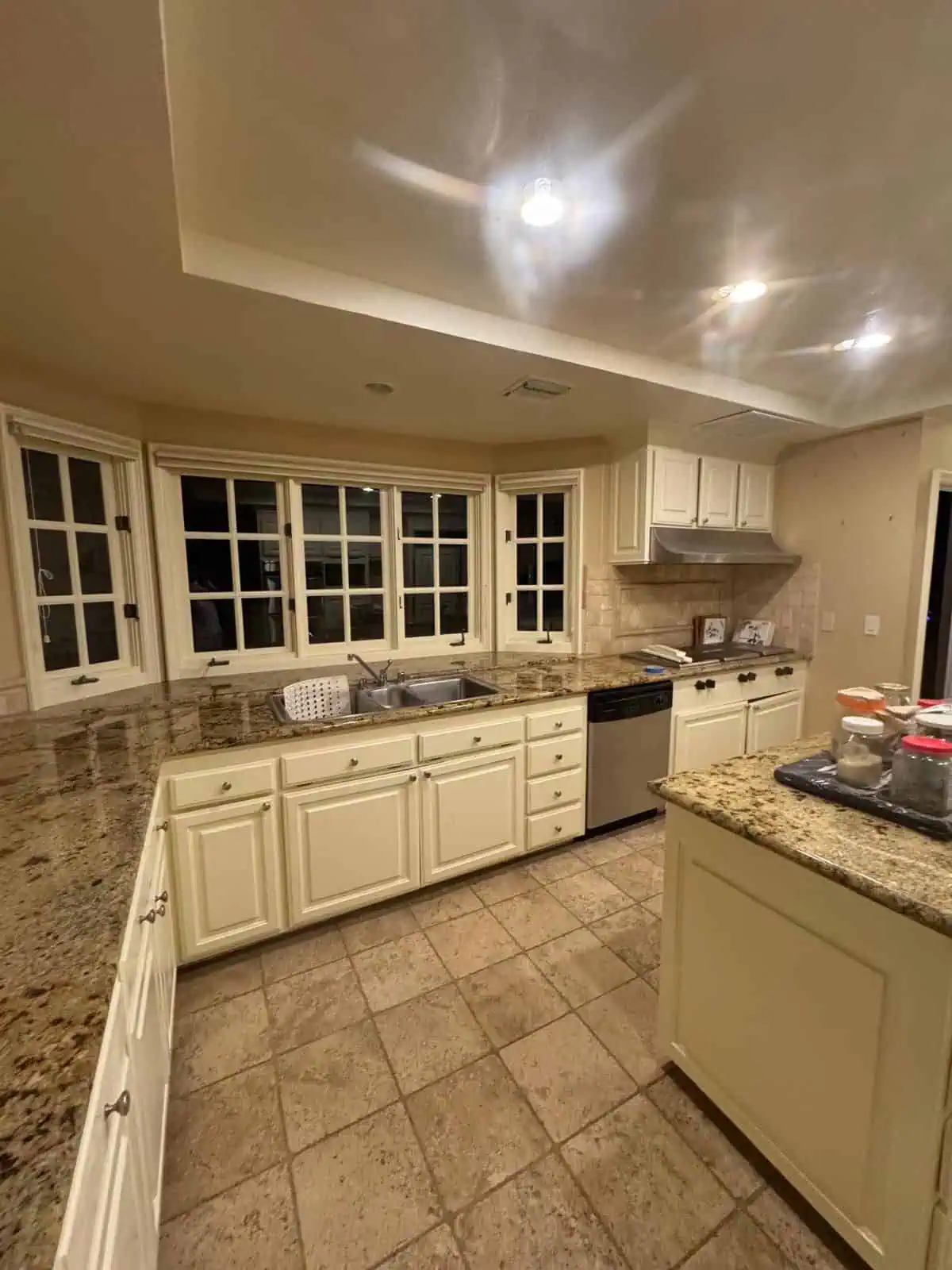 Kitchen with white cabinets, granite countertops, and large bay windows at night.